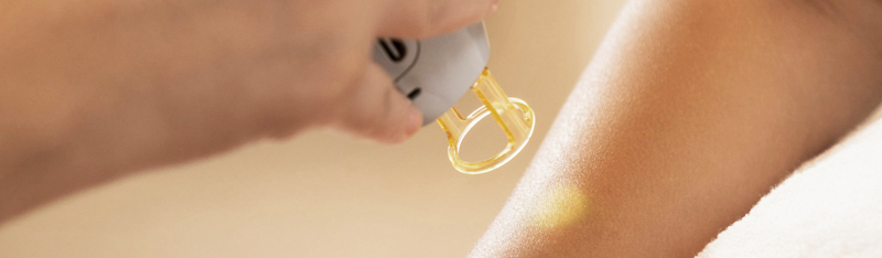 A person receiving a laser facial treatment with a handheld device emitting blue light, held by a gloved professional in a clinical setting.